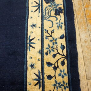 Navy rug with a thick, yellow floral border featuring blue vines rests on light wood plank flooring.