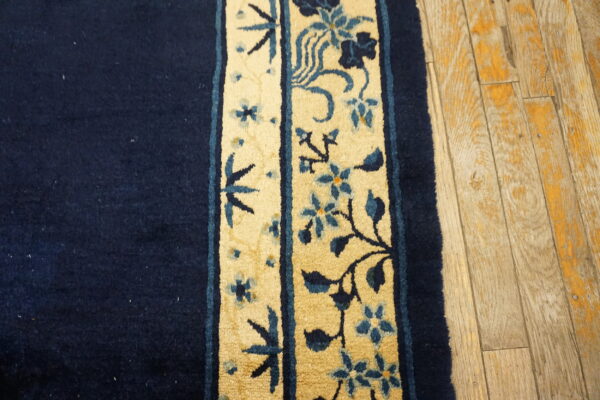 Navy rug with a thick, yellow floral border featuring blue vines rests on light wood plank flooring.
