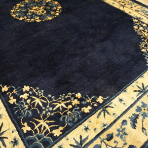 A detailed view of a dark blue rug with wide gold borders featuring stylized blue and gold florals.