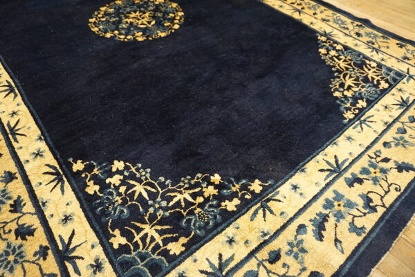 A detailed view of a dark blue rug with wide gold borders featuring stylized blue and gold florals.
