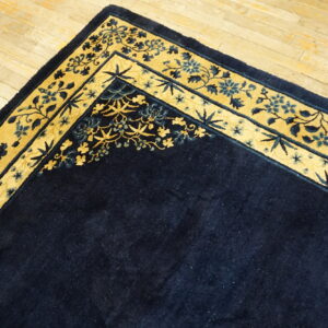 A dark blue rug with a gold and blue ornamental border is displayed on light plank wood floors.