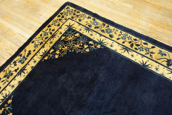 A dark blue rug with a gold and blue ornamental border is displayed on light plank wood floors.