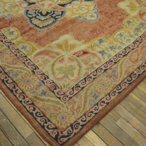 Sculpted floral and scrollwork rug in pale blue, salmon, and cream lies on distressed wood flooring.
