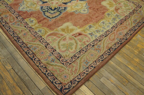 Sculpted floral and scrollwork rug in pale blue, salmon, and cream lies on distressed wood flooring.