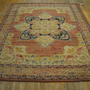 Rectangular rug with a rust field, cream medallion, and elaborate floral border on distressed wood flooring.