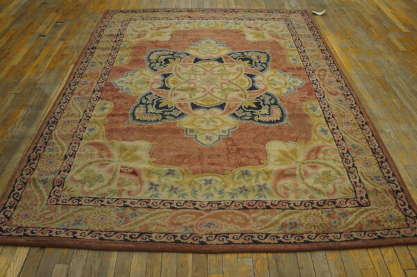 Rectangular rug with a rust field, cream medallion, and elaborate floral border on distressed wood flooring.