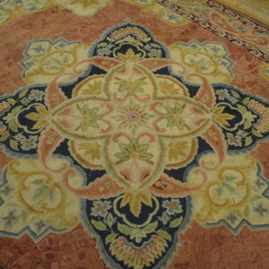 Detail of a pinkish-red rug showing a large floral medallion in navy, cream, and green on a wood floor.