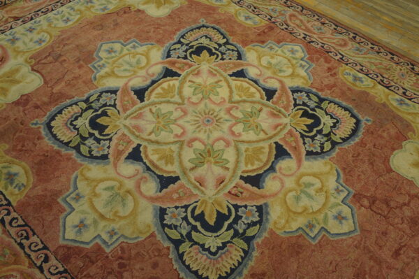 Detail of a pinkish-red rug showing a large floral medallion in navy, cream, and green on a wood floor.