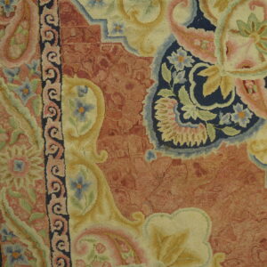 High-textured, floral rug in rust, navy, cream, and pale pink rests against rustic wood planks.