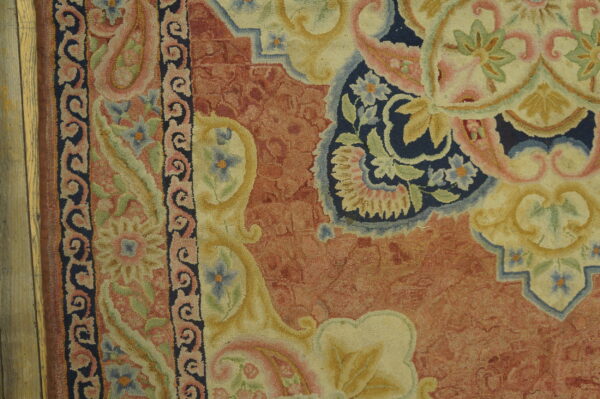 High-textured, floral rug in rust, navy, cream, and pale pink rests against rustic wood planks.