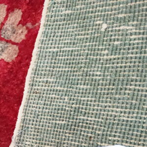 The contrast between the red floral rug pile and its woven teal and white grid backing.