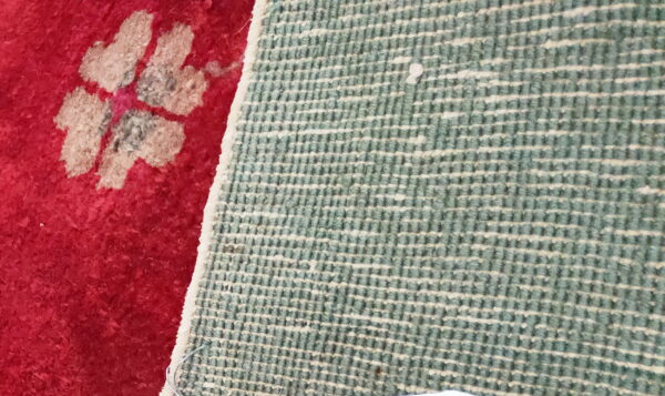 The contrast between the red floral rug pile and its woven teal and white grid backing.