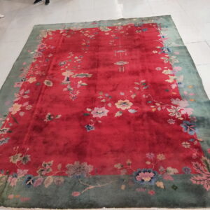 A crimson and green floral rug lies on white tiled flooring, with the feet of surrounding people visible.