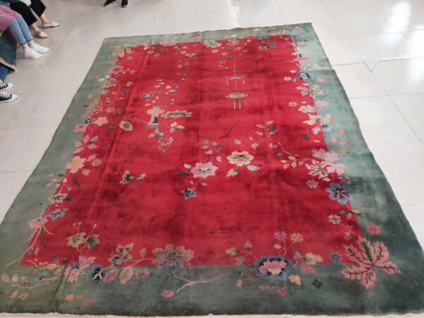 A crimson and green floral rug lies on white tiled flooring, with the feet of surrounding people visible.