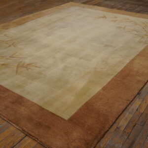 A muted beige and brown rug with bamboo foliage patterns rests on distressed wooden floorboards.
