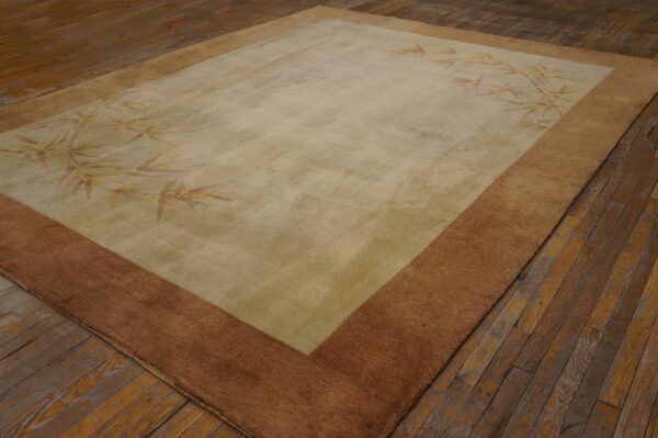 A muted beige and brown rug with bamboo foliage patterns rests on distressed wooden floorboards.