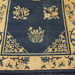 Navy blue rug with tan and light blue floral designs and a wide tan border on wood flooring.