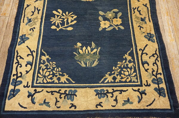 Navy blue rug with tan and light blue floral designs and a wide tan border on wood flooring.