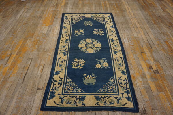 A narrow blue rug with cream and green floral patterns rests on distressed wooden floors.