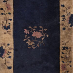 Rectangular rug with a dark blue field and a wide beige border patterned with scrolling pink and navy flowers.