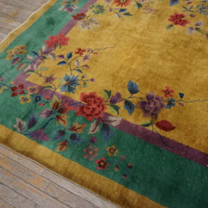 Mustard yellow rug with a green and purple border featuring multicolored floral details on distressed wood floors.