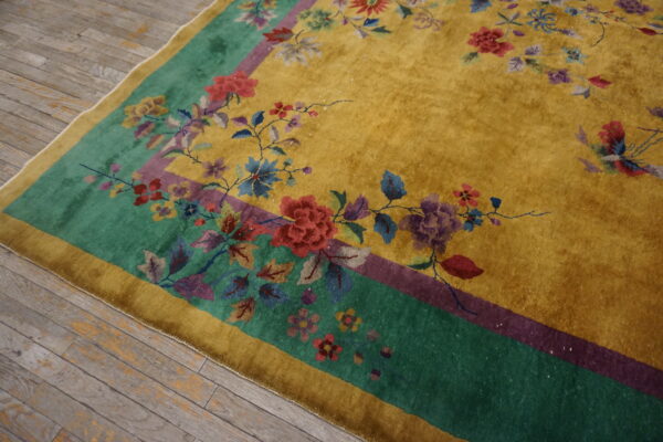 Mustard yellow rug with a green and purple border featuring multicolored floral details on distressed wood floors.