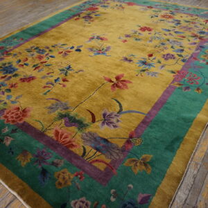 Mustard yellow rug with high pile and detailed multicolor floral pattern, bordered in teal and purple, lying on distressed wood floor.
