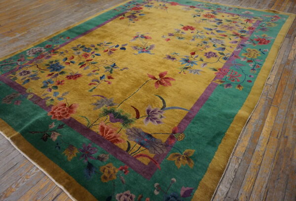 Mustard yellow rug with high pile and detailed multicolor floral pattern, bordered in teal and purple, lying on distressed wood floor.