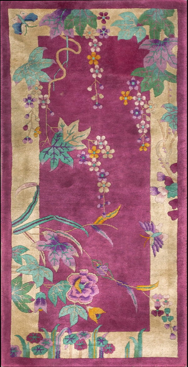 Long fuchsia rug with tan borders decorated with cascading vines and purple, green, and yellow flowers.