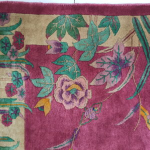 Plush magenta rug featuring a flowing floral pattern in beige, teal, purple, and pink, with visible fringe.