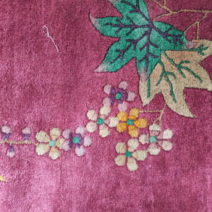 Magenta rug texture with a colorful pattern of maple leaves and tiny yellow, purple, and green flowers.