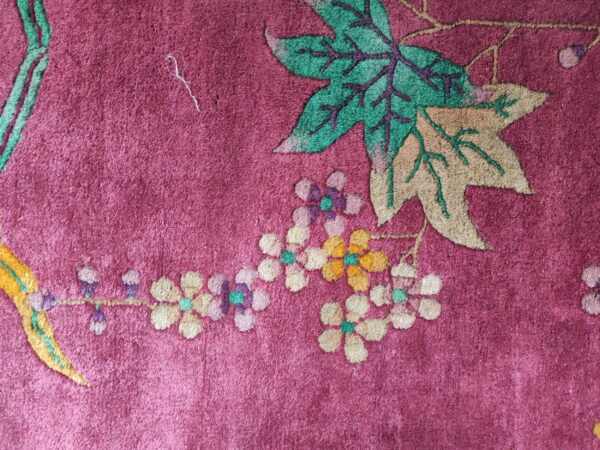 Magenta rug texture with a colorful pattern of maple leaves and tiny yellow, purple, and green flowers.
