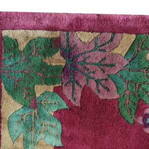 Textured magenta rug close-up with large carved green and pink leaf designs and a beige patterned border.