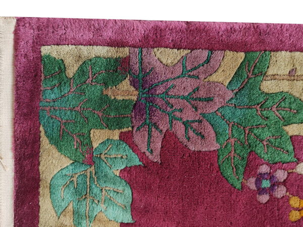 Textured magenta rug close-up with large carved green and pink leaf designs and a beige patterned border.
