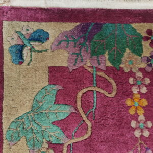 Magenta and tan high-pile rug detail showing large green leaves, colorful flowers, and a blue butterfly motif.