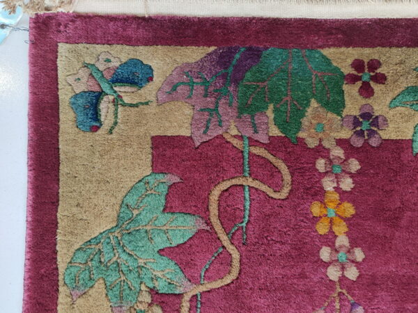 Magenta and tan high-pile rug detail showing large green leaves, colorful flowers, and a blue butterfly motif.