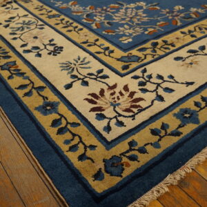 A blue floral rug featuring cream and gold borders rests on distressed natural hardwood flooring.