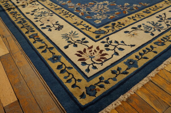 A blue floral rug featuring cream and gold borders rests on distressed natural hardwood flooring.