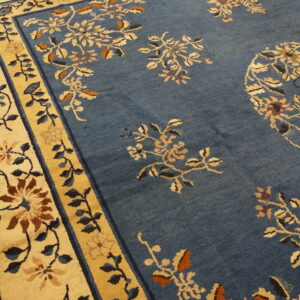 Close-up of a dusty blue rug with tan, cream, and brown floral patterns and wide yellow borders.