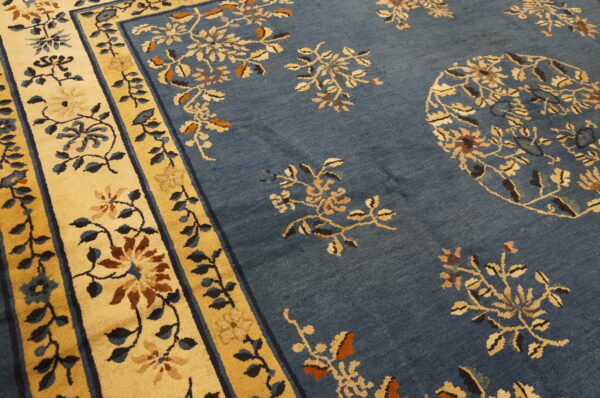 Close-up of a dusty blue rug with tan, cream, and brown floral patterns and wide yellow borders.