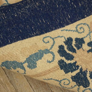 Dark blue, light blue, and beige patterned rug corner folded back over light wooden floor.