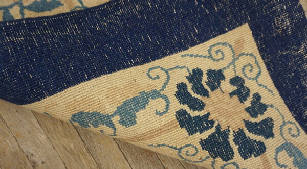 Dark blue, light blue, and beige patterned rug corner folded back over light wooden floor.