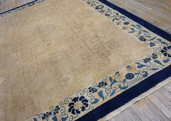 A beige rug with subtle patterns and a blue floral border rests on distressed wooden floorboards.