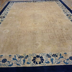 Tan rug featuring a subtle geometric field design and a prominent blue floral border on wood planks.