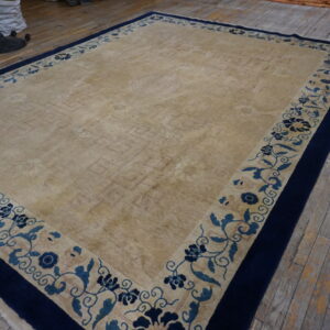 Large beige area rug with a navy blue and light blue floral border on rustic wood planks.