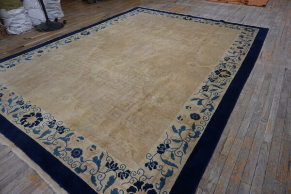 Large beige area rug with a navy blue and light blue floral border on rustic wood planks.