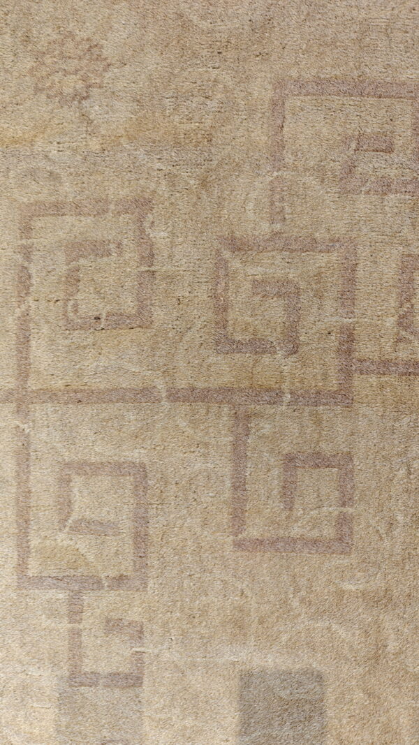 Tan high-pile rug detail showing a distressed pattern of light brown interlocking geometric borders.