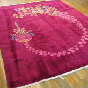A rectangular deep berry rug with multi-colored floral designs rests on wood plank flooring.