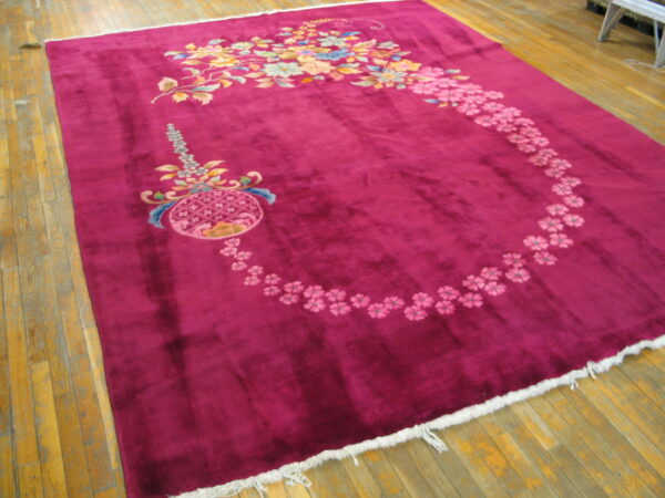 A rectangular deep berry rug with multi-colored floral designs rests on wood plank flooring.