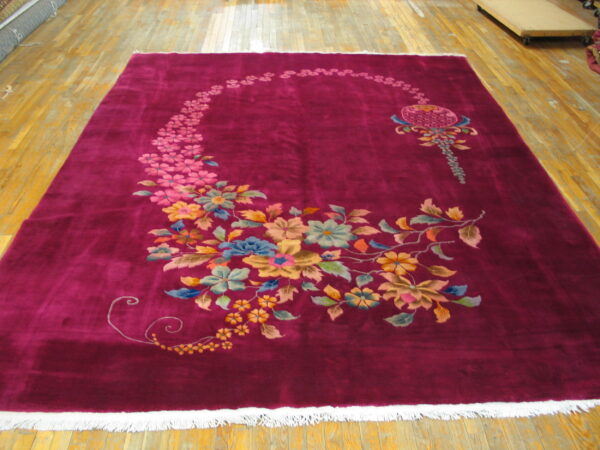 Deep magenta rug with white fringe featuring a curving multicolor floral design on bare wood floors.